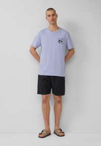 Lichtpaarse t-shirt met korte mouwen en zwarte grafische print op de borst, gecombineerd met zwarte shorts en bruine sandalen. Eenvoudig en casual ontwerp.