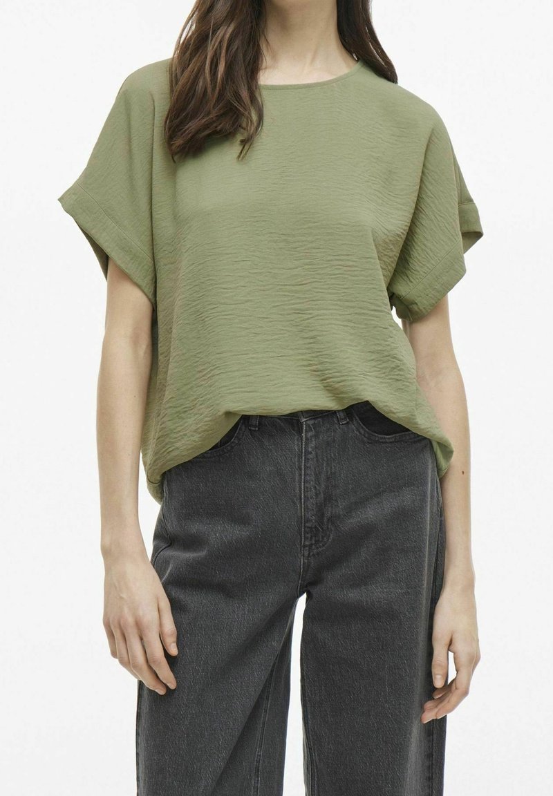 Top verde con maniche corte e trama, con scollo rotondo, abbinato a jeans a gamba larga color grigio scuro a vita alta. Tessuto morbido e leggero.