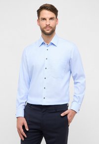 Camicia azzurro chiaro con bottoni, realizzata in tessuto dalla texture liscia, con taschino sul petto, bottoni scuri e maniche lunghe.