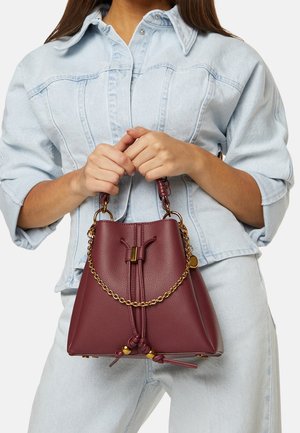 Sac seau en cuir bordeaux avec des accents en chaîne dorée et une fermeture à cordon. Présente une finition douce et texturée ainsi qu'une base structurée.