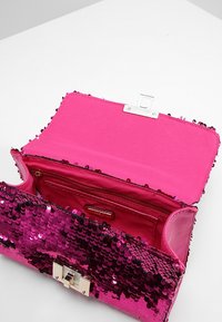 Vaaleanpunainen paljettikäsilaukku kiiltävällä viimeistelyllä, läppäkiinnityksellä ja sisäisellä vetoketjutaskulla. Sileä materiaali, jossa on teksturoitu, paljeteilla koristeltu ulkopinta.