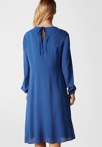 Abito blu con finitura testurizzata, maniche lunghe e dettaglio a forma di occhiello sul retro. Presenta una vestibilità comoda e arriva fino a metà polpaccio.