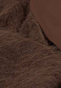 Brauner, flauschiger Stoff mit Struktur, übereinandergelegt mit einem glatten, leicht glänzenden braunen Material. Es sind keine auffälligen Muster oder Akzente sichtbar.