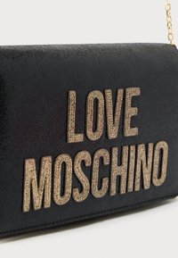 Μαύρη υφασμάτινη τσάντα χειρός με χρυσές επιγραφές "LOVE MOSCHINO". Διαθέτει λουρί αλυσίδα και λείο φινίρισμα. Προσφέρει μοντέρνο και κομψό στυλ.