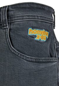 Dunkelgraue Denim-Jeans mit einem auffälligen, in Orange und Blau gestickten "homeboy x-tra"-Logo auf der Gesäßtasche.