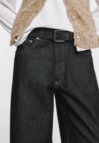 Fekete farmer egyenes szárú kialakítással, kontrasztos fehér varrással, első zsebekkel és fekete övvel. Texturált világos pulóver rétegben.