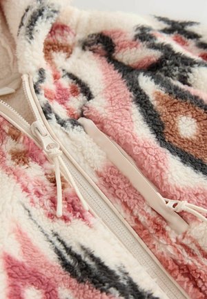 Primo piano di un morbido tessuto in pile con motivi rosa, marroni, neri e bianchi e una zip beige con cordini.