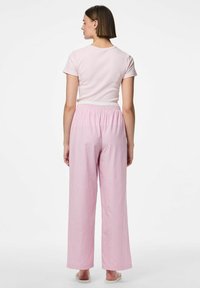 Kerge roosa lühikeste varrukatega pluus, mis on sobitatud laia lõikega roosa ja valge triibuliste pükstega, millel on elastne vöökoht ja sirged jalad.