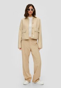 Beige cropped blazer met knoopsluiting en twee voorzakken, gecombineerd met lichtbruine gestreepte wijde broek en witte sneakers.