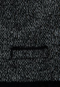 Tissu texturé noir et gris avec un gros plan sur une ouverture de poche fendue horizontale centrée dans le cadre.