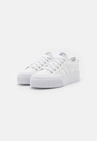 Λευκά αθλητικά παπούτσια Adidas με χαμηλή εφαρμογή, επίπεδες σόλες, κορδόνια και τρεις χαρακτηριστικές ρίγες στις πλευρές, τοποθετημένα σε λευκό φόντο.