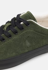 Gröna mockaskor med svarta snören, gummisula och präglad logotypdetalj. Texturerad yta med kontrasterande krämfärgade foder.