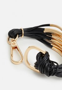 Bracelet en cuir noir avec quincaillerie dorée, comprenant un clip et des accents métalliques décoratifs. Texture douce avec des détails tressés.