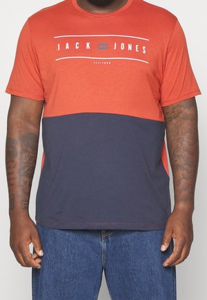 Mand iført en kortærmet t-shirt med rød øverste halvdel, navy nederste halvdel og teksten "JACK JONES" hen over brystet.