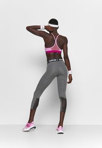 Leggings grigi con vita nera e dettagli in mesh, abbinati a un reggiseno sportivo rosa con schiena in mesh. Sneakers bianche e rosa completano il look.