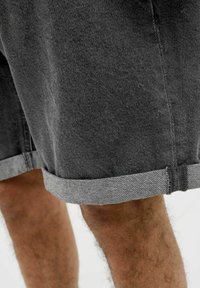 Shorts en denim gris avec un ourlet replié, présentant un tissu texturé et des détails de couture gris clair. Ils offrent une coupe décontractée et une longueur au milieu des cuisses.