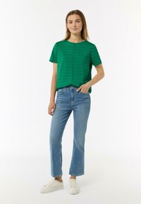 Green striped short-sleeve top with a round neckline, paired with light blue jeans and white sneakers. Simple design, relaxed fit.