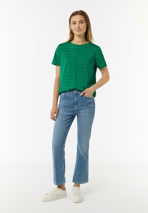 Green striped short-sleeve top with a round neckline, paired with light blue jeans and white sneakers. Simple design, relaxed fit.