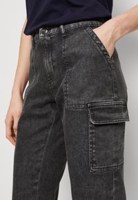 Schwarze Cargo-Jeans mit lockerer Passform, ausgestattet mit Seitentaschen, dezenten Verwaschungen und sichtbaren Nähten an Bund und Taschen.
