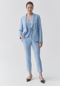 Svijetloplavi odijelo s krojenim sakoom i suženim hlačama. Ima dva gumba na sakou i elegantan dizajn. Upareno s tamnim cipelama na špic.