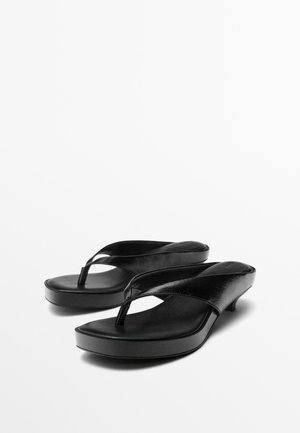 Paire de sandales noires en cuir avec lanière en forme de tongs, petits talons aiguilles bas et plateformes légèrement surélevées, présentées sur fond blanc.