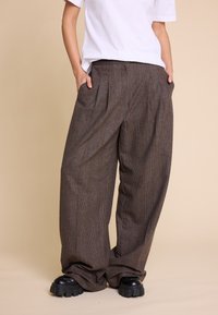 Brune rutete vide benbukser med frontfolder, lavt liv og sidelommer, kombinert med kraftige svarte platåsko.