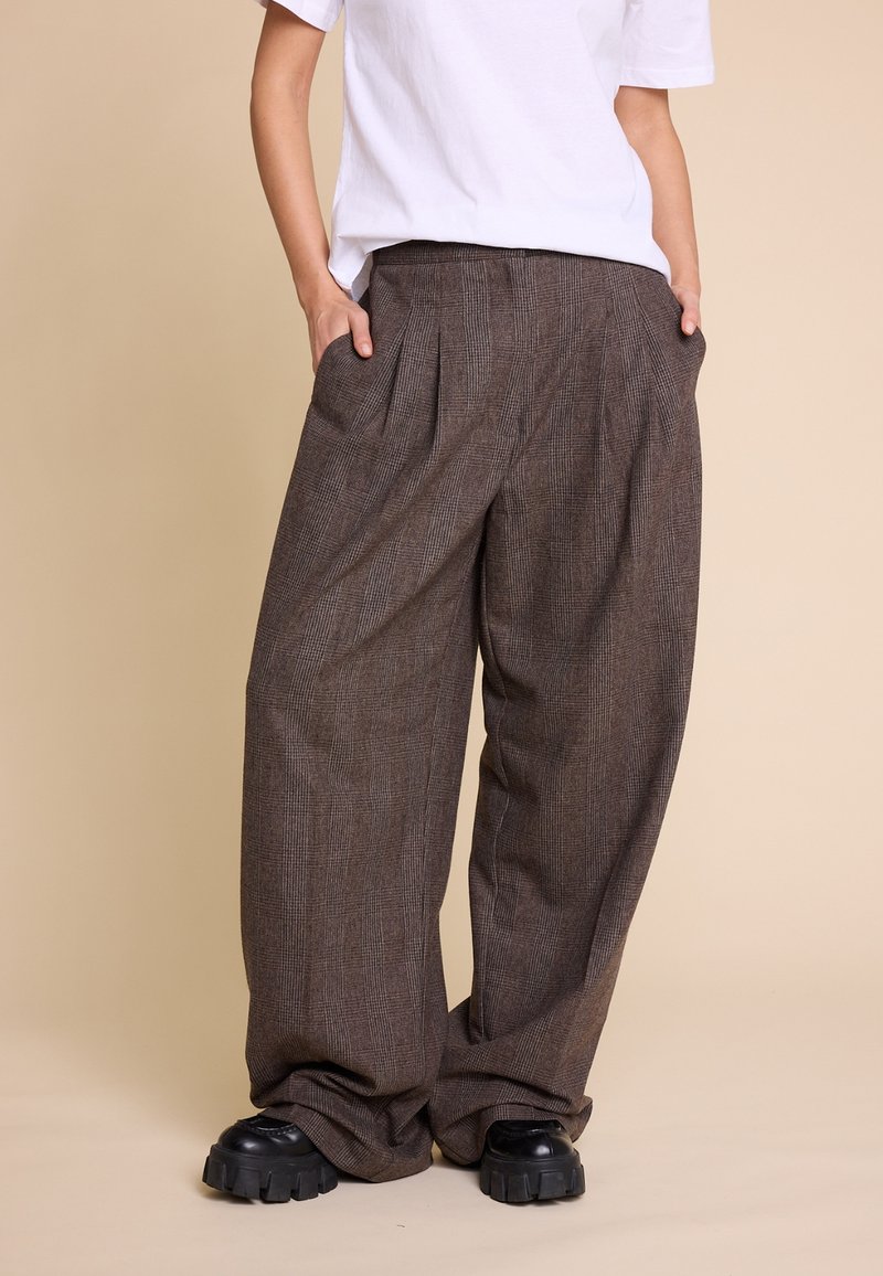 Brune rutete vide benbukser med frontfolder, lavt liv og sidelommer, kombinert med kraftige svarte platåsko.