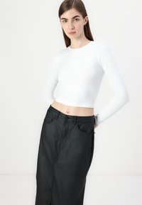 Fehér, hosszú ujjú crop top, mely egy magasan derékig érő fekete farmer szoknyával van párosítva, elülső hasítékkal és látható varrási részletekkel.