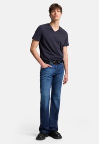 Marinblå V-ringad t-shirt kombineras med blå denimjeans med rak passform och ett svart bälte. Svarta skor fulländar outfiten.