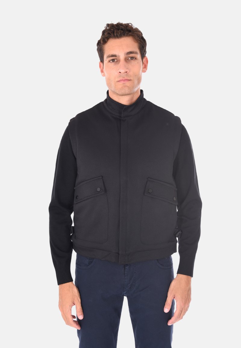 Giacca nera con colletto alto, spalle strutturate, due tasche frontali e polsini a coste. Presenta un tessuto testurizzato e una vestibilità sartoriale.