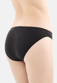 Slip in cotone nero con una texture liscia, design a vita bassa e cuciture sottili in vita e alle aperture delle gambe.