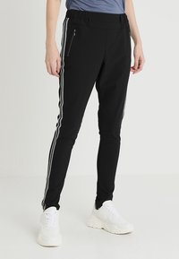 Zwarte sportieve broek met een elastische tailleband, zijritsen en witte strepen langs de zijkanten, gemaakt van een glad, flexibel materiaal.