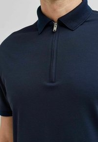 Námornícky polo tričko s polovičným zipsom, s textúrovaným golierom a hladkým materiálom, navrhnuté pre priliehavý vzhľad.