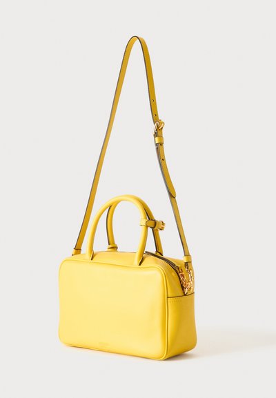 Sac à main rectangulaire jaune avec deux petites poignées et une longue bandoulière réglable, présenté sur un fond clair uni.