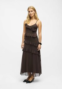 Robe maxi marron avec des volants superposés, des bretelles spaghetti et un design fluide. Associée à des chaussures à talons noires. Tissu lisse et léger.