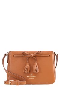 Ruskea nahkainen olkalaukku, jossa on sileäpintainen rakenne, rusettiyksityiskohta ja kaksi hapsua. Edessä kullanvärinen logo ja säädettävä olkahihna.