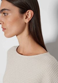 Beige strukturierter Pullover mit weitem Ausschnitt und geripptem Stoff, der dezente metallische Fäden für zusätzliche Details enthält.