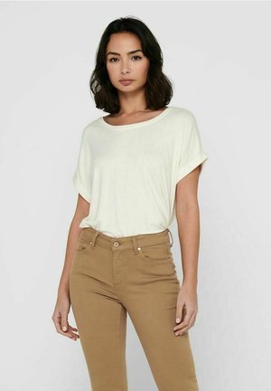 Ljus krämfärgad t-shirt i lös passform med uppvikta ärmar, bärs tillsammans med bruna tajta jeans. Den övergripande texturen verkar slät och bekväm.