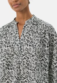 Blusa a fiori in bianco e nero con colletto alla cinese, dotata di una placca frontale e realizzata in un tessuto leggero. Vestibilità rilassata e texturizzata.