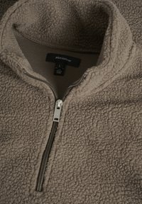 Pullover in pile con zip metà, di colore marrone chiaro, caratterizzato da un esterno testurizzato, un interno liscio e dettagli in cerniera argentata. Etichetta del marchio inclusa.