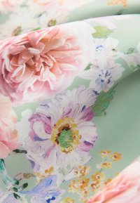 Blommande tyg med en pastellgrön bakgrund som har stora rosa pioner och mindre tusenskönor. Mjuk textur och livliga färger.