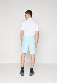 Light blue shorts with a smooth texture, back pockets, and a subtle logo. Worn with a white polo shirt and dark footwear.