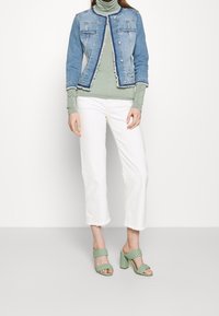 Jeansjacka med rå fåll, ljusblå färg; lager på lager med en grön polokrage, vita avkortade jeans och gröna vävda klacksandaler.