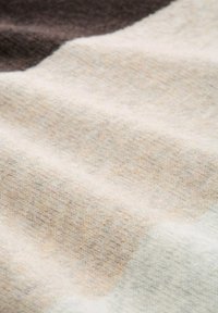 Tessuto texturizzato in morbido beige e strisce marroni attenuate, che mostra un motivo a maglia con spessore variabile e sottili transizioni di colore.