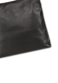 Sac à main en cuir noir avec une surface texturée sur fond blanc, montrant un coin et une partie de la bandoulière.