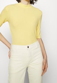 Gul kortærmet top med høj hals, lavet af et blødt strikstof. Sættet inkluderer lyse jeans med forreste knap og lommer.