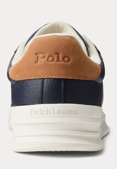 Δερμάτινο αθλητικό παπούτσι σε ναυτικό μπλε με ταμπελάκι τακουνιού από καφέ σουέντ που φέρει ανάγλυφο το λογότυπο "Polo" και λευκή σόλα με ανάγλυφο το "Ralph Lauren", σε θέα από πίσω.