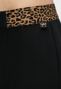 Κοντινό πλάνο μαύρου παντελονιού με φαρδύ λωρίδα μέσης με λεοπάρ μοτίβο και μικρό ταίριασμα ετικέτας θηλιάς στο πλάι.