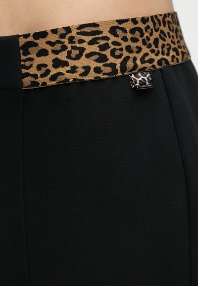 Gros plan sur un pantalon noir avec une large taille à imprimé léopard et une petite étiquette boucle assortie sur le côté.