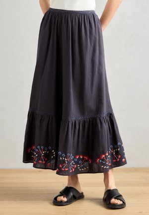 Gonna in cotone di un blu navy scuro con un design a strati, caratterizzata da ricami floreali colorati all'orlo e un girovita arricciato. Abbinata a sandali neri a scivolo.